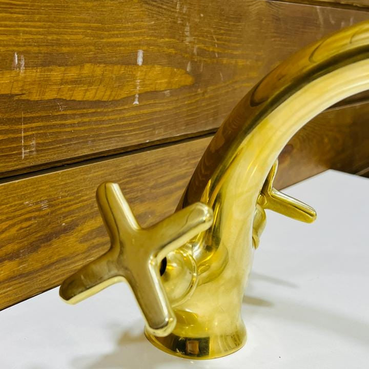 Close-up of classic cross handles on an unlacquered brass bathroom faucet