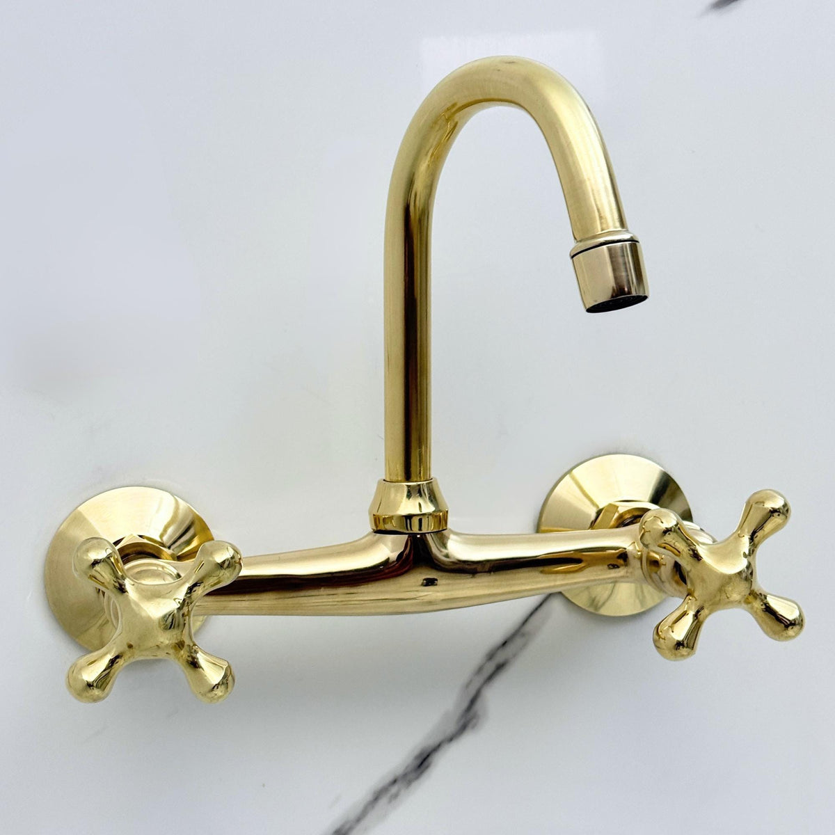 Close-up of cross handles on an unlacquered brass wall mounted faucet