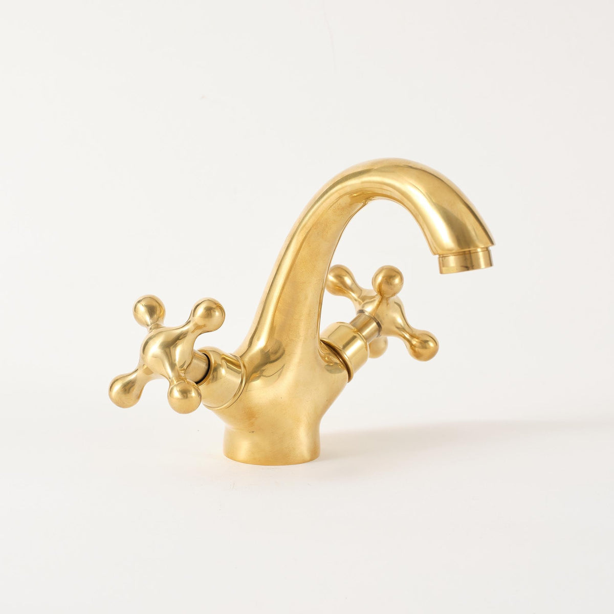 Close-up of unlacquered brass bathroom faucet highlighting handcrafted brass finish and cross handles